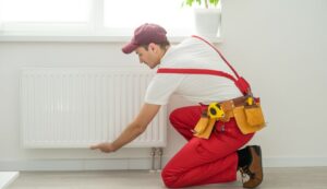 un homme en tenue de travail en train d'installer un radiateur dans une maison.