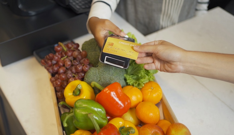 Une personne payant ses fruits et légumes par carte bleue à la caisse.