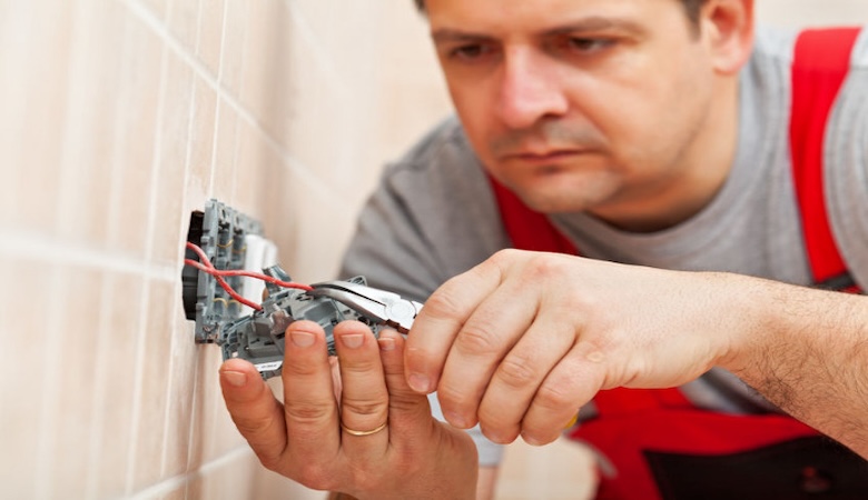 Un électricien travaillant sur une prise électrique murale.